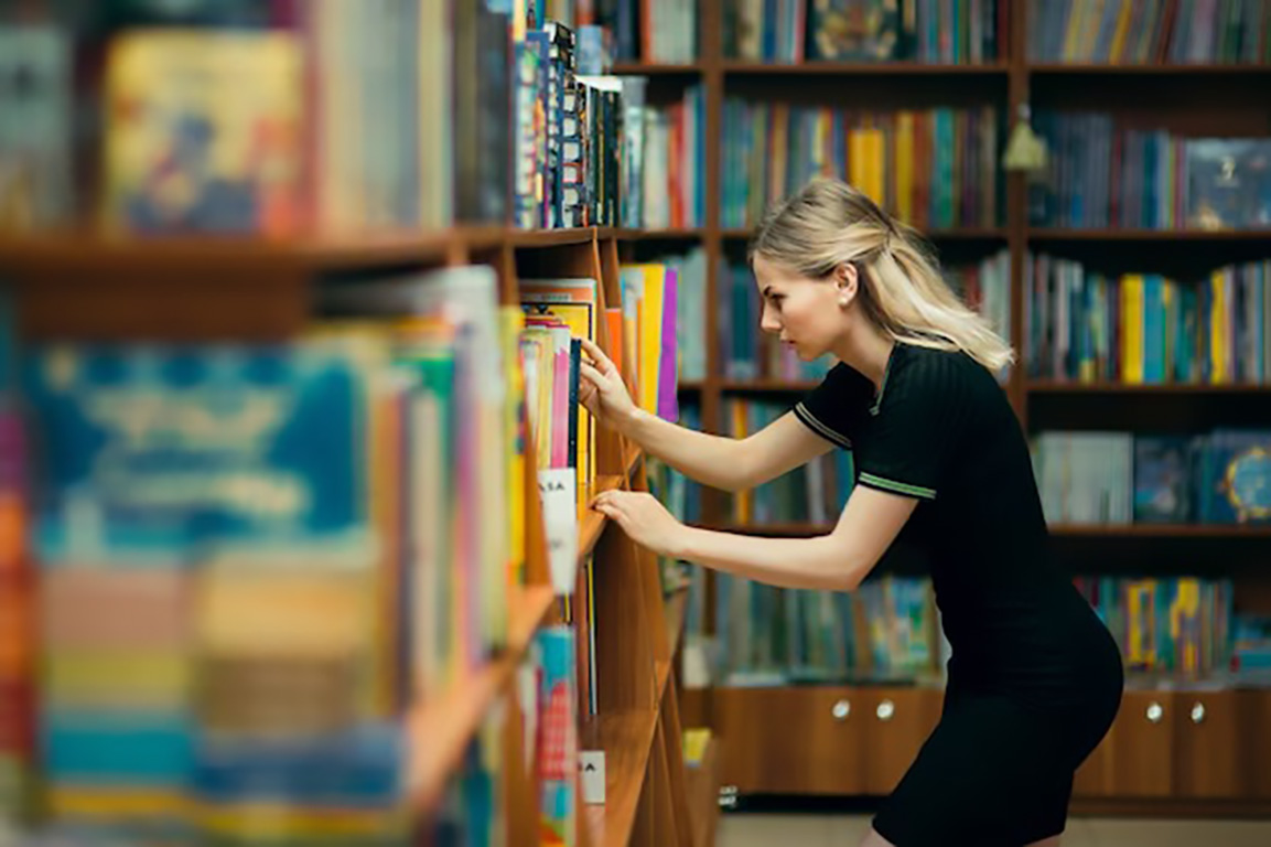 a woman looking for a book in a bookshelf of a library